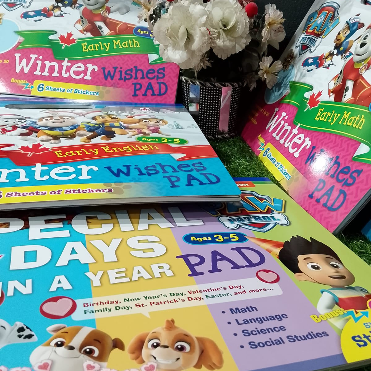 Educational books for children on a grassy surface with flowers in the center.