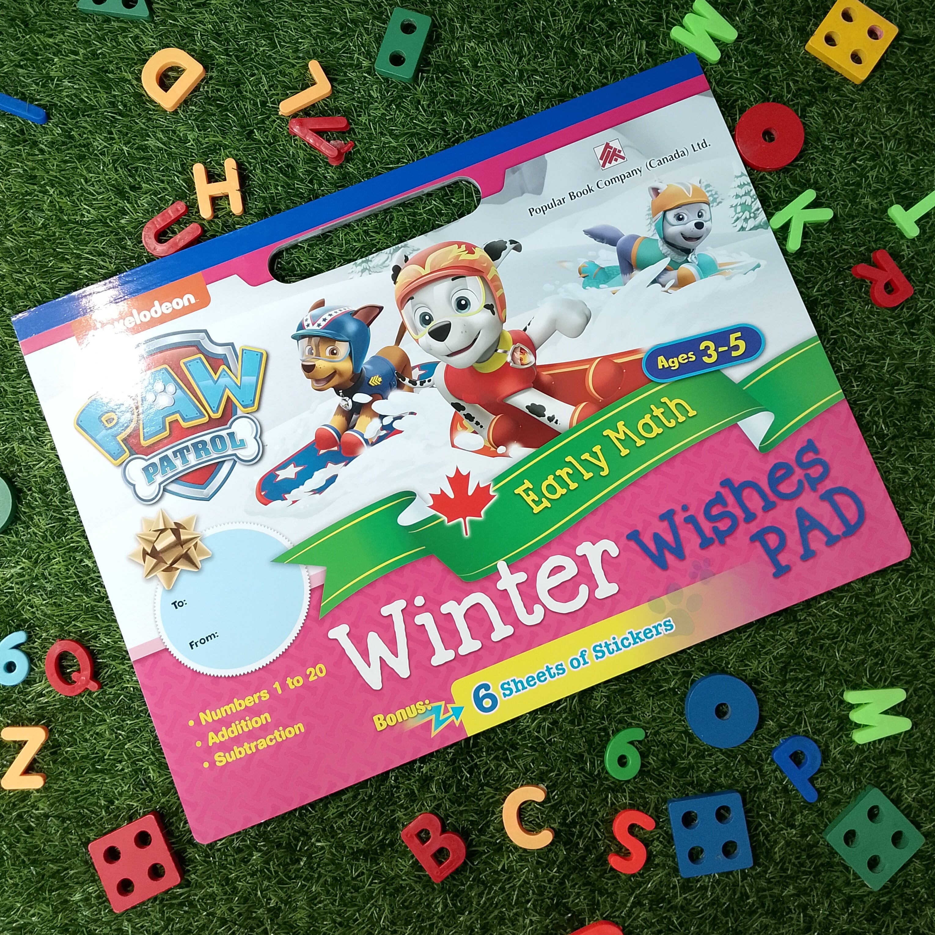 Children's activity book titled 'Early Math Winter Wishes Pad' by Paw Patrol on a grass background with colorful letters and numbers.