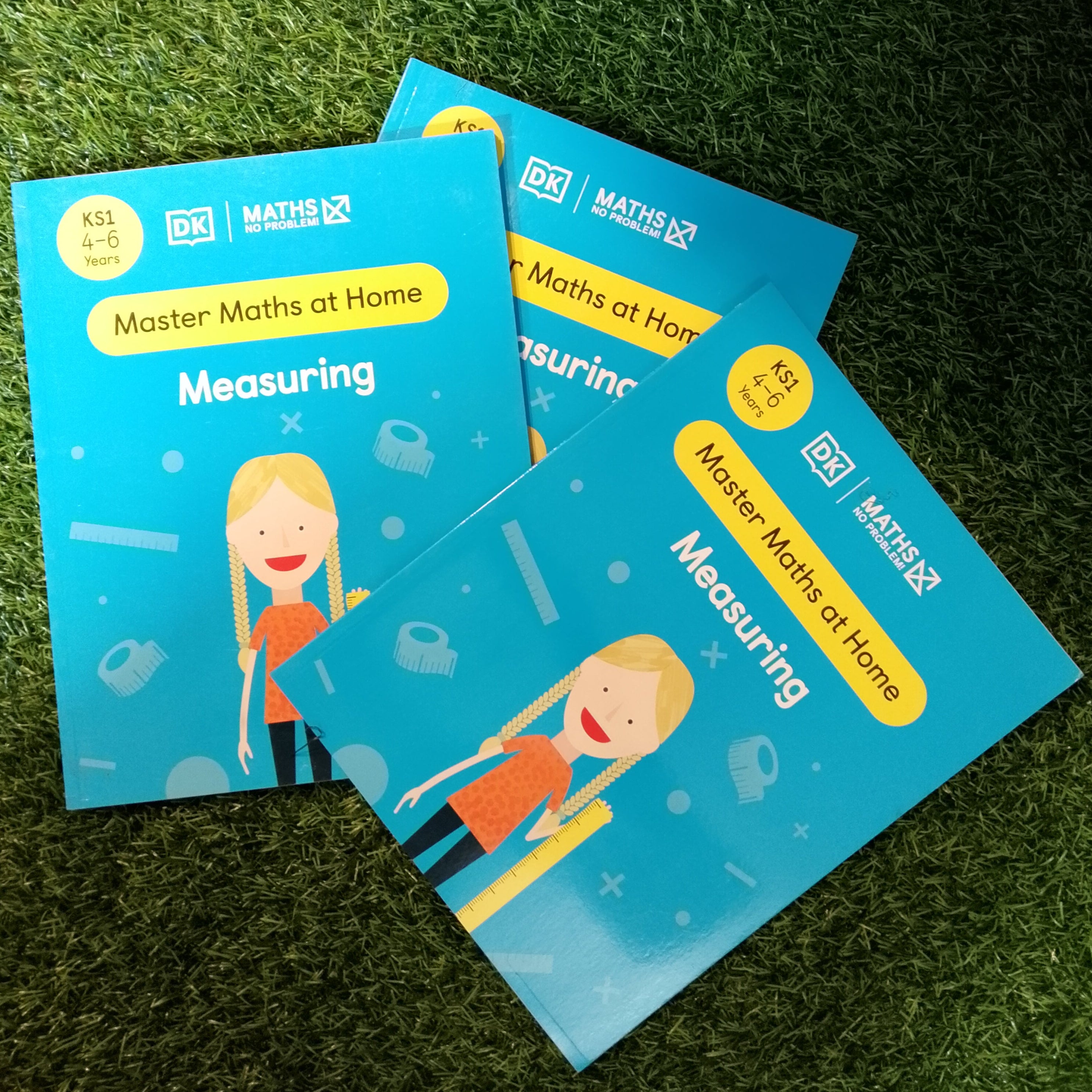 Three 'Master Maths at Home' books on a grassy background